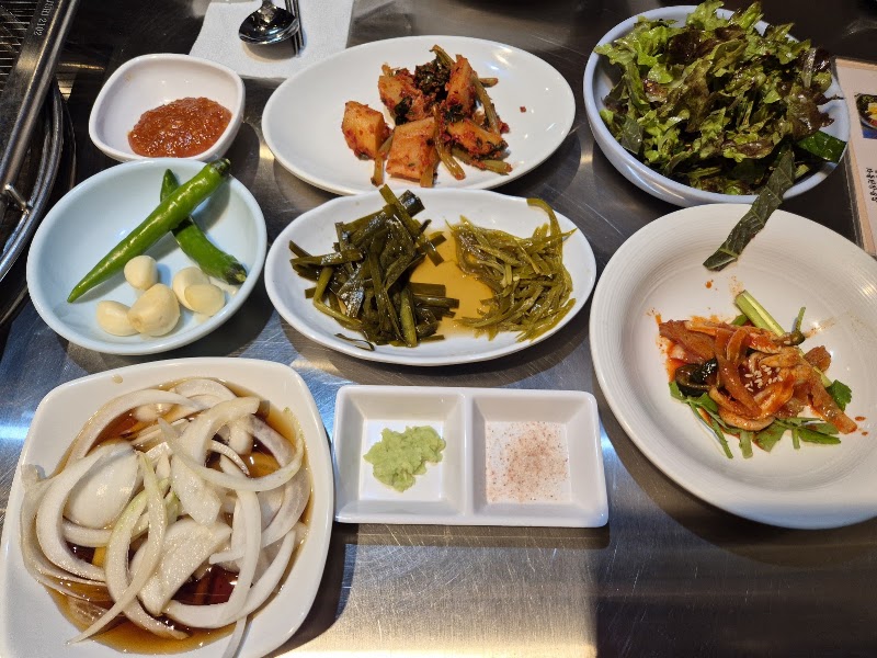 Banchan side dishes with kimchi, seasoned vegetables, onions, and dipping sauces