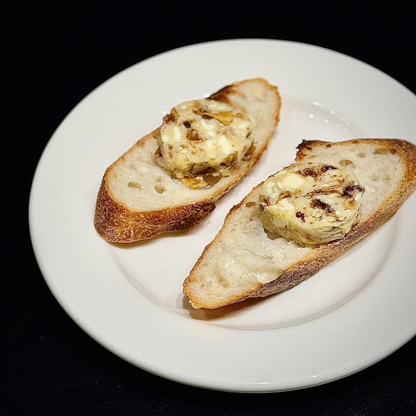 Two slices of toasted baguette topped with herb or fruit-infused butter on a white plate