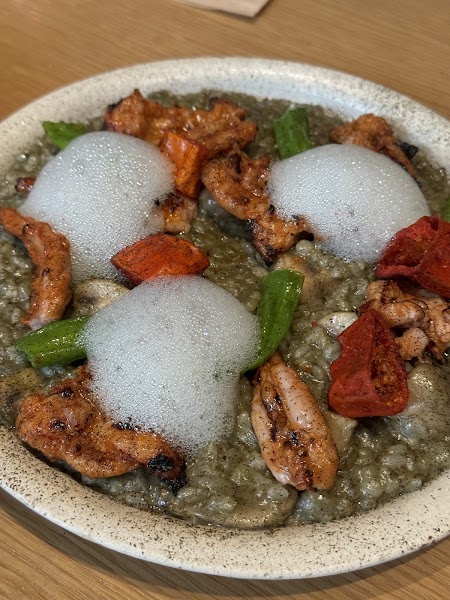 Dark textured risotto topped with seared meat cuts, vegetables, and airy culinary foam