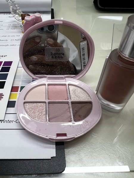 Open eyeshadow palette labeled Euphoria next to cosmetic bottle on personal color analysis worksheet