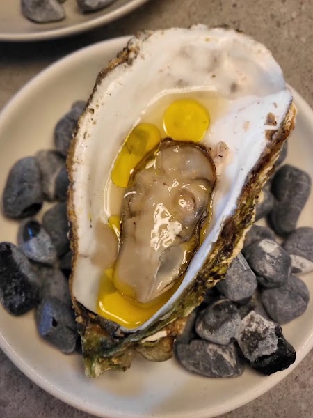 Fresh oyster on the half shell served on smooth dark pebbles with golden oil