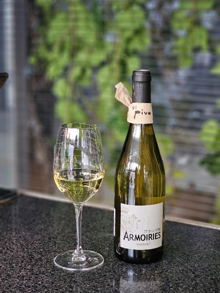 A wine bottle with a Pivo tag and a glass of white wine on a dark granite counter