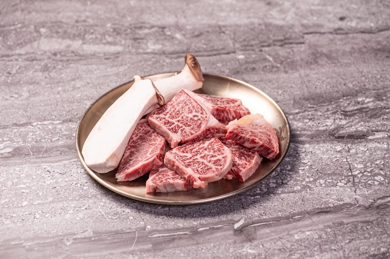 A metal plate with raw marbled beef and king oyster mushrooms on a gray marble tabletop.