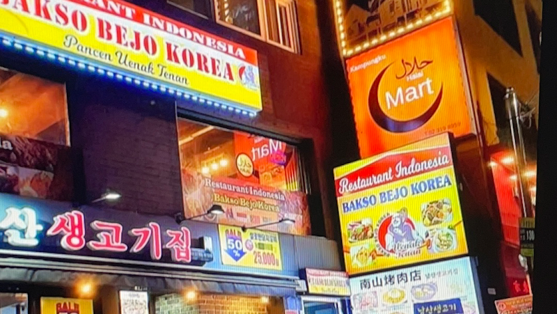 Exterior view of the illuminated signs of Bakso Bejo Korea restaurant and Kampungku Mart at night in Myeongdong