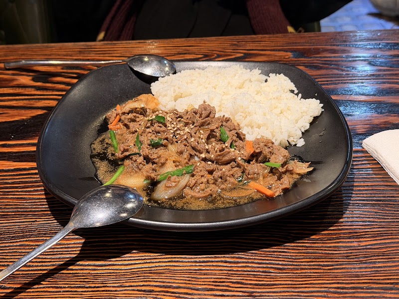 Bulgogi beef with sliced carrots and onions served with white rice on a black plate