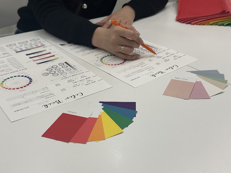 A personal color consultant using an orange pen to mark results on a diagnostic color chart at a desk with color swatch fans