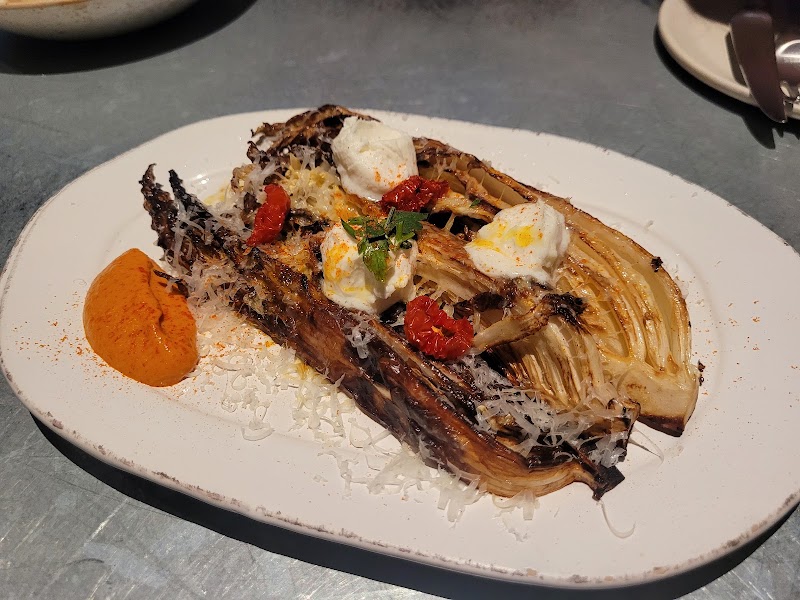 Flame-roasted cabbage wedges topped with cheese, sun-dried tomatoes, and savory sauce on a metal table