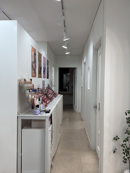 A narrow, modern white hallway in a consultant's studio featuring shelves filled with various cosmetics and makeup products.