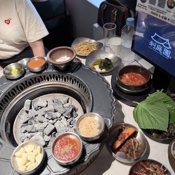 A close-up view of a Korean barbecue grill table with various side dishes and charcoal coals at Lee Jung Won restaurant in Seoul.