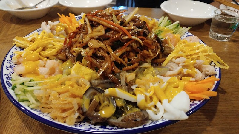 A colorful plate of Chinese cold noodle dish with shredded vegetables, seafood, egg strips, and mustard sauce at a restaurant.