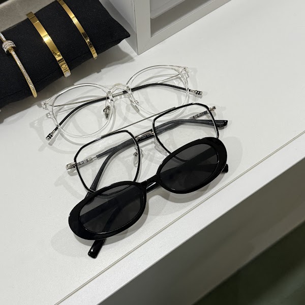 Three pairs of glasses stacked on a white surface with gold bracelets in the background