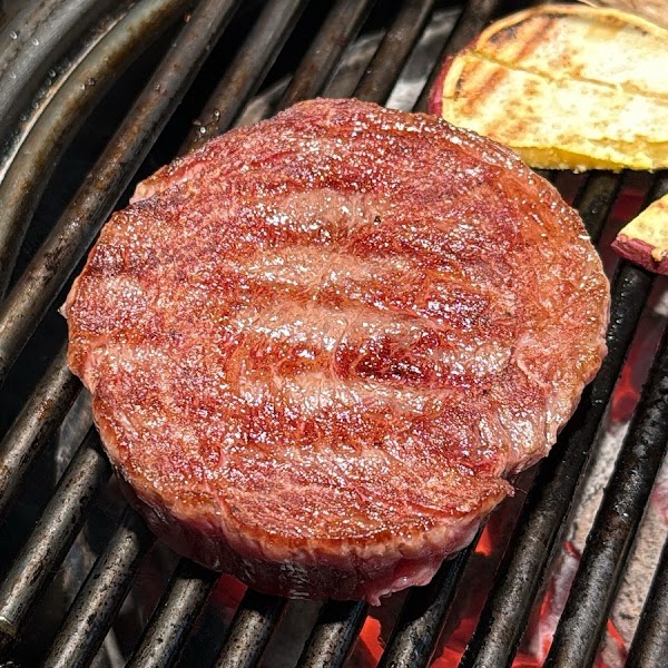 A raw, round piece of steak grilling on a metal barbecue rack.