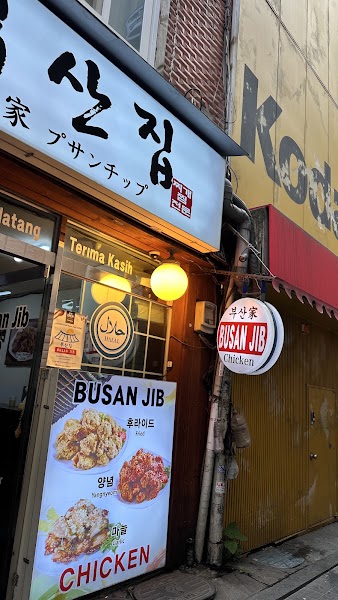 Storefront of Busan Jib restaurant in Seoul with a glowing illuminated sign and a menu poster featuring fried chicken