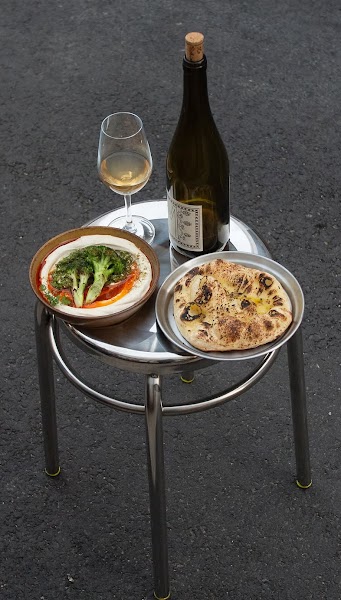 Metal stool holding a ceramic bowl of roasted vegetables, toasted bread, and wine bottle