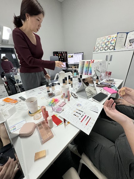 A consultant during a personal color analysis session with makeup products and color palettes on a desk.