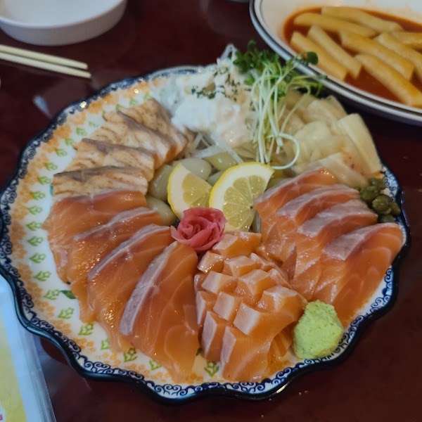 A platter of sliced raw salmon, seared salmon, and garnishes served on a scalloped edge plate at a restaurant.