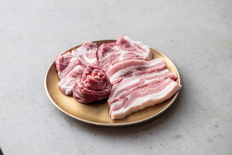 Raw pork cuts on a gold plate on a grey stone table.