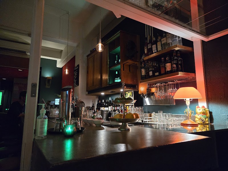 Dimly lit interior showing bar back shelves, glassware, and warm lamp next to a golden lucky cat figurine