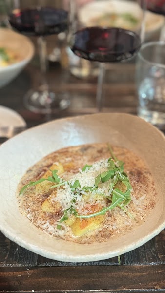 Off-white ceramic bowl filled with golden gnocchi in rich cream sauce topped with arugula and cheese