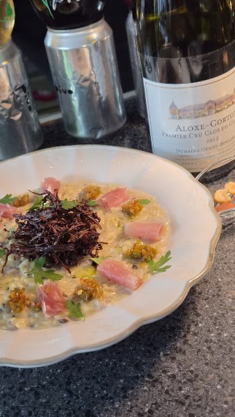 A gourmet dish featuring risotto, cured meat, and dark crispy garnish served with wine