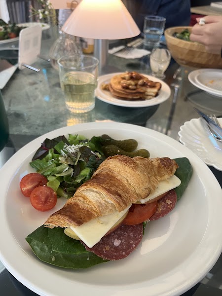 Crisp croissant sandwich filled with salami, cheese, and fresh greens, served with side pickles