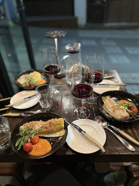 Plates of grilled cabbage topped with cherry tomatoes and herbs served beside glasses of red wine