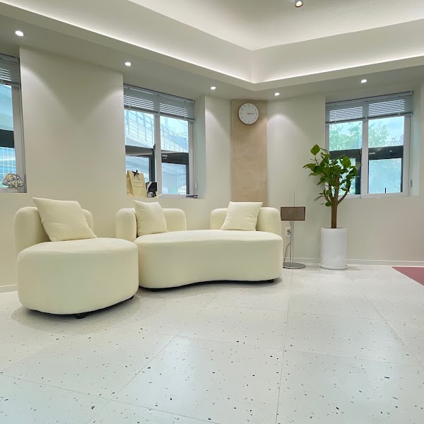 A clean, modern waiting area with curved white furniture, indoor plants, and soft recessed lighting in a personal color consulting studio