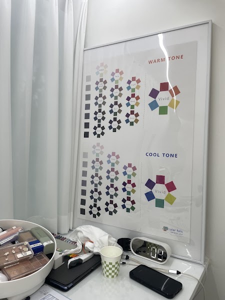 A framed personal color analysis chart showing warm and cool tone palettes hanging on a white wall above a makeup station