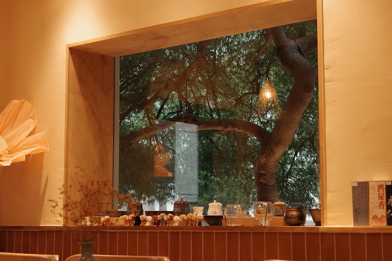 A large window in Dadam Tea House looking out at a lush tree, with small ceramic tea ware and animal figurines on the sill.