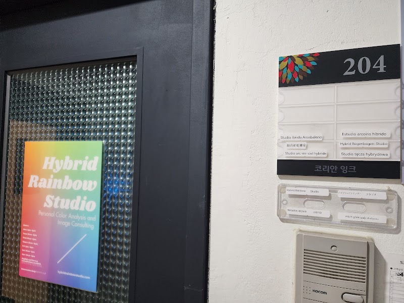 Entrance to Hybrid Rainbow Studio featuring a colorful sign on a glass door and office directory on a white wall.