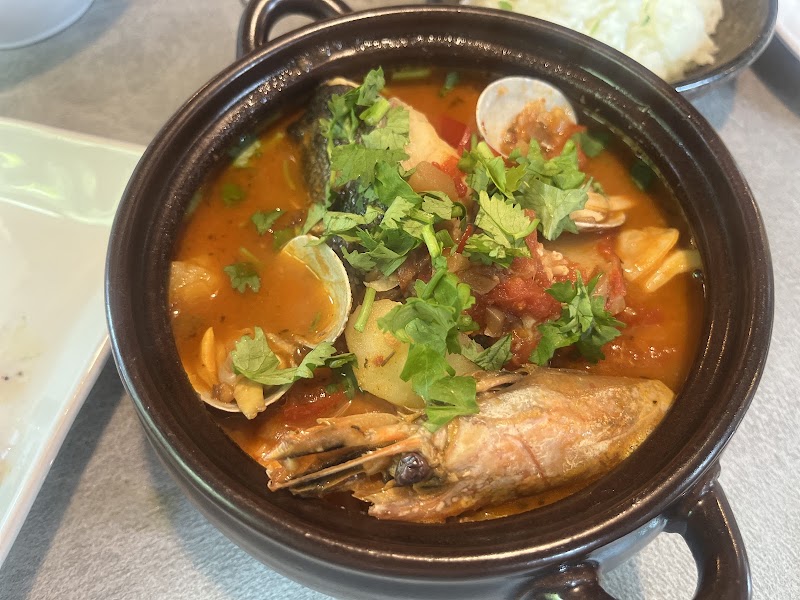 A bowl of Portuguese fish stew with shrimp clams and herbs in a dark ceramic pot