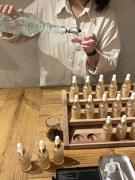 A person pouring liquid from a clear patterned glass bottle into a small measuring cup at a perfume studio.