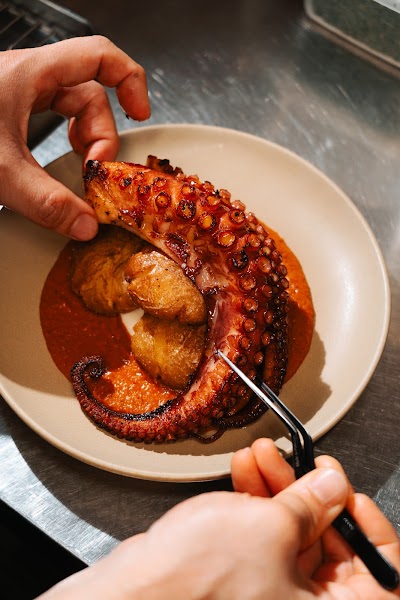 Chef carefully plating the grilled octopus with potatoes and paprika sauce