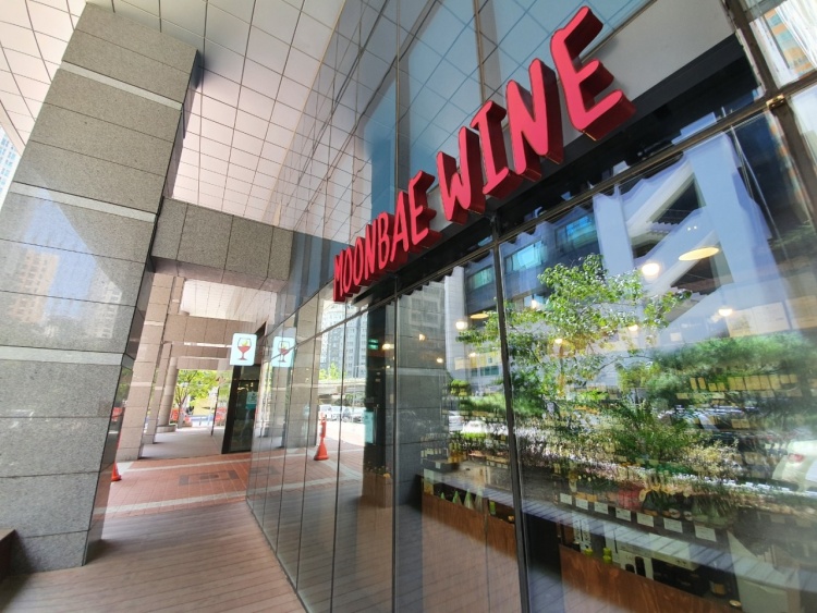 Exterior view of Moonbae Wine store entrance featuring red lettering and a glass facade