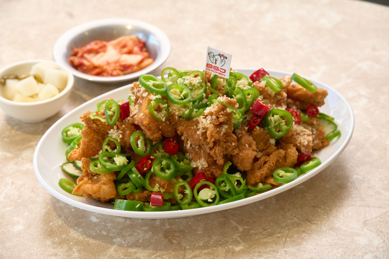 A plate of fried chicken topped with green and red chili peppers and minced garlic, served with side dishes at a restaurant.
