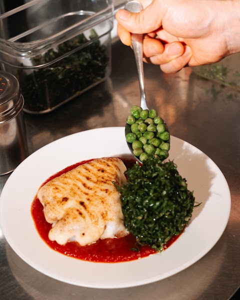 Chef spooning sweet green peas onto a fresh seafood plate in the kitchen
