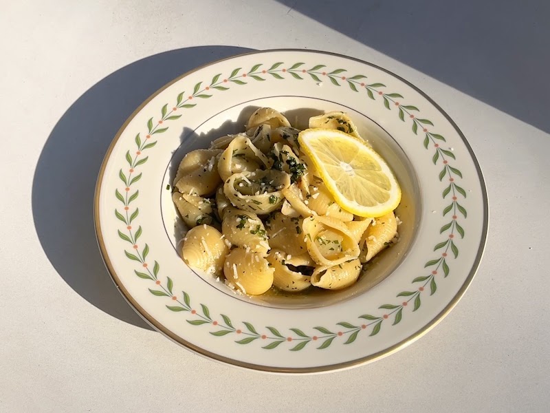 Herbed shell pasta with fresh lemon slice and aromatic garnishes in an artisanal bowl