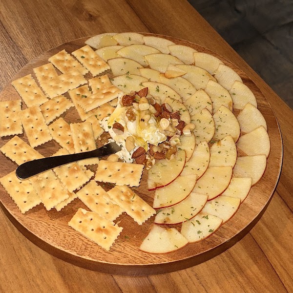 Round wooden platter with sliced apples, crackers, cream cheese, nuts, and honey