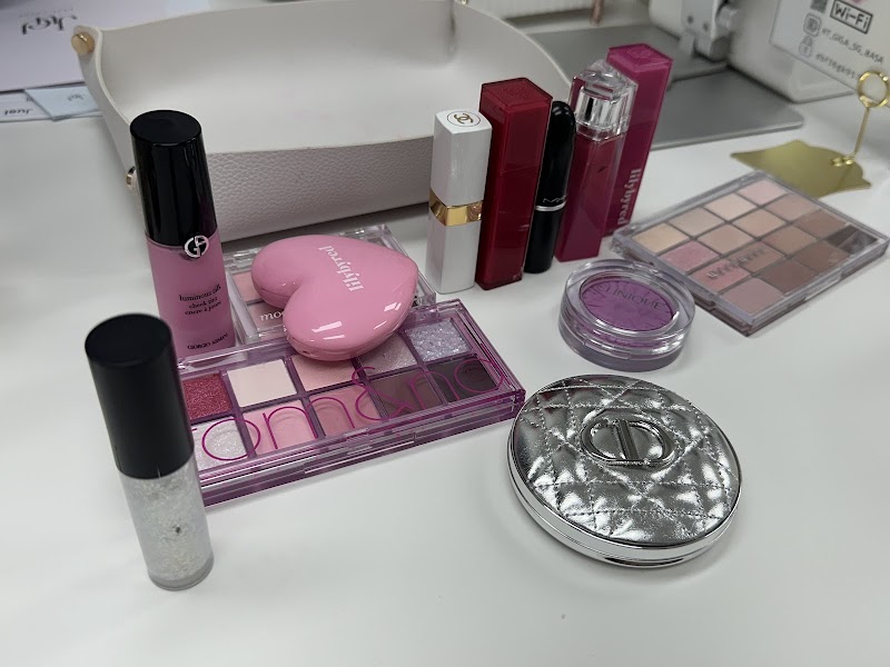 A collection of makeup products including eyeshadow palettes, lipsticks, and compacts on a white desk.