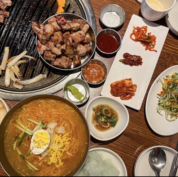 A bird's-eye view of a Korean barbecue table featuring grilled meat, noodle soup, and various side dishes.