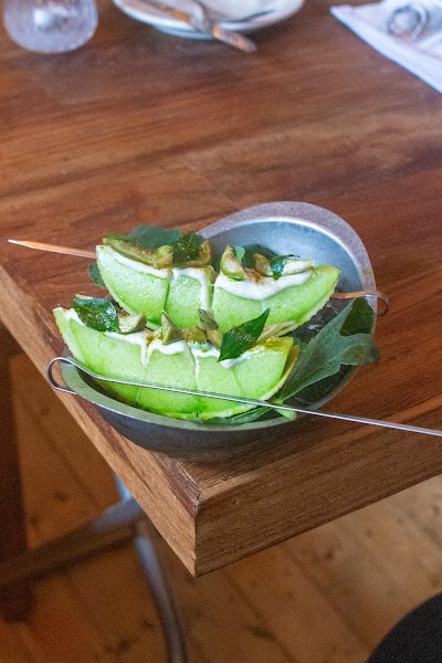 Melon skewers topped with cream sauce and herbs in a stainless steel bowl on wood