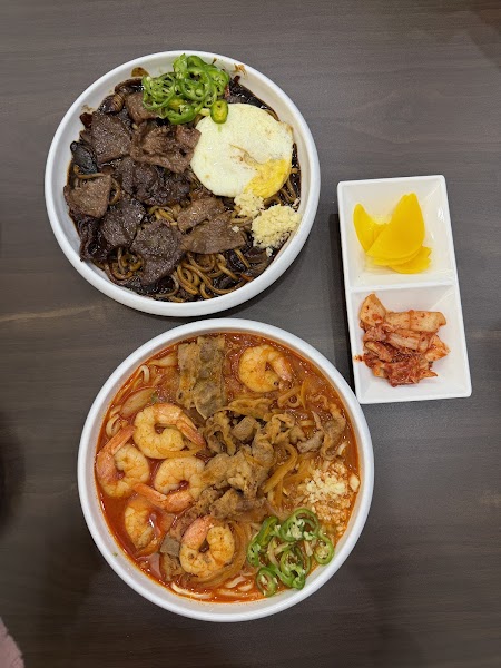 Two bowls of noodles and side dishes on a wooden table at BSJ Chicken & WOK in Seoul.