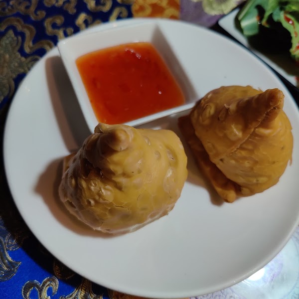 Two golden fried samosas served on a white plate with a side of red dipping sauce