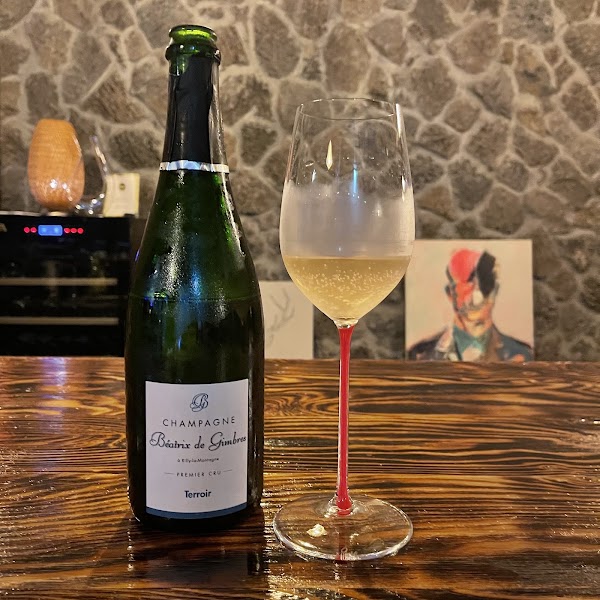 Béatrix de Gimbres Champagne bottle and crystal glass against rustic basalt stone wall at Andante Vino
