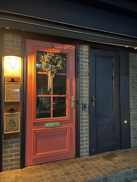 The exterior entrance of Bistro Oven and Vine featuring a pink door with a wreath and an adjacent dark blue door at night.