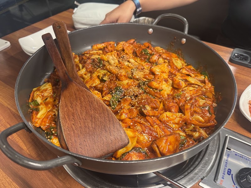 Large pan of seasoned Dakgalbi chicken with wooden spatulas