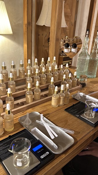 A perfume making workspace featuring rows of essential oil vials, beakers, and digital scales on a wooden table.