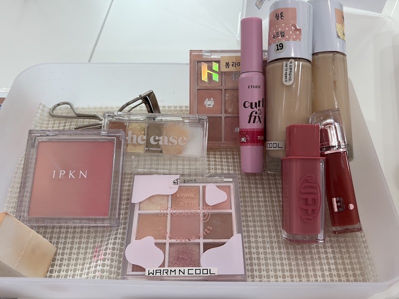 Collection of various cosmetic products in a clear plastic bin used for color consultation.