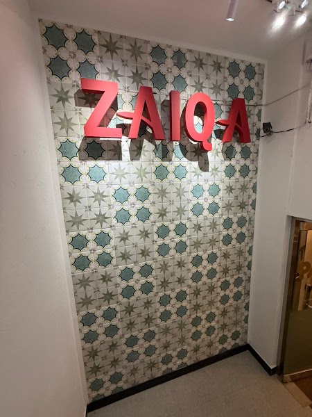 Decorative patterned tile wall with red illuminated Zaiqa signage