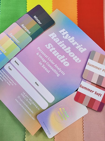 Hybrid Rainbow Studio promotional card with color season palettes and fabric swatches on a desk.